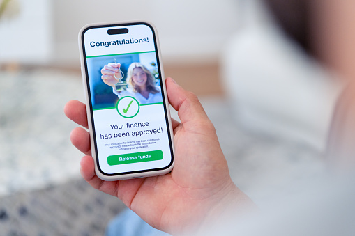 Man holding a mobile phone with mortgage loan application approval. There is an image on the phone of a woman with a house key. Close up.