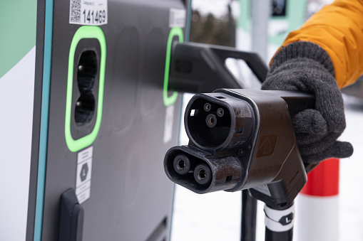 man holding DC charging connector in hand, pfalzwerke electric vehicle CCS2 quick-charge station, alternative energy in winter, technology and innovation, Frankfurt - January 21, 2024