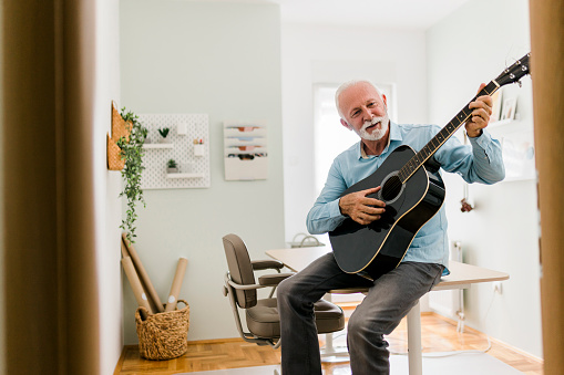Senior male playing guitar at home office
