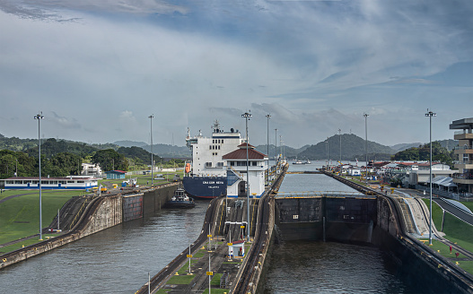 Panama Canal, Panama - July 24, 2023: Miraflores locks 2 chambers northbound with a tugboat and CMA CGM Neva container ship. Green landscape under blue cloudscape