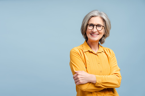 Elegant mid adult woman against white background. Stylish mature woman in blue casuals looking at camera and smiling.