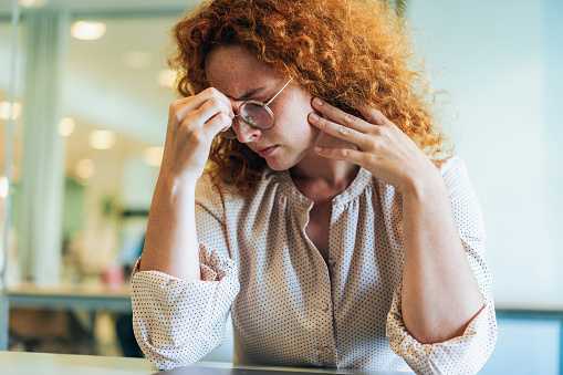 Business woman with hands on her head looking exhausted. Tired Business woman sitting in front of laptop at the office having headache. Frustrated businesswoman