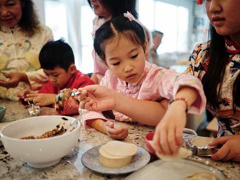 An extended Chinese family spending time together on Chinese New Year, making jiaozi dumplings in a home kitchen.