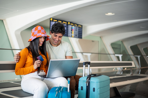 young couple with credit card and laptop buying their flight at the airport with luggage copy space