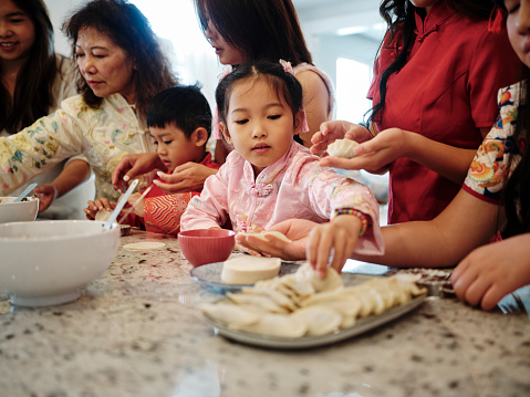 An extended Chinese family spending time together on Chinese New Year, making jiaozi dumplings in a home kitchen.