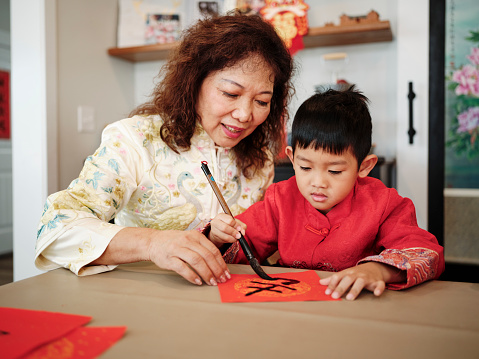 An extended Chinese family practicing calligraphy for Chinese New Year, writing Fai Chun messages with traditional paint and brush.