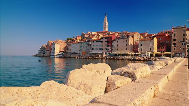 SLO MO Shot of Harbor and Historic Buildings by Sea against Blue Sky on Sunny Day in Rovinj. Istra, Croatia.