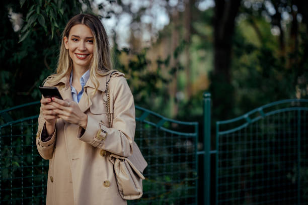 istock A stylish woman is using her phone outdoors, smiling at the camera. 2013811813