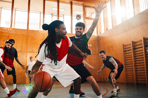 Interracial professional basketball players playing basketball on training at indoor court. Multicultural experienced sportsmen in action with on basketball court. A sportsman is dribbling a ball.