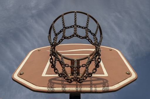 Edinburgh, Scotland, Jan 19, 2024 - View of Basketball backboard with the hoop metal ring and steel chain net against blue sky background seen from below. Street basketball court, Low angle view, Look up, Space for text, Selective focus.