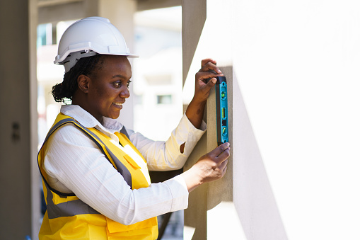 Professional American - African black ethnicity engineer using the water level meter measure balance of the building parts. Female engineer or foreman uses water level measurement ruler.