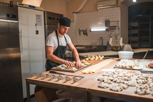 Caucasian artisan baker working in a small bakery. Shaping pastries and setting them up on a baking tray.