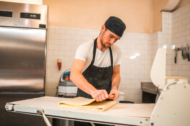 istock Artisan Baker Folding Dough On A Dough Sheeter In A Small Bakery 2013826308