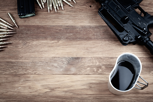 assault rifle and cup of coffee on wooden table background