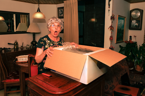 A senior Colombian lady shows surprise and excitement opening a gift from her son. It is a toaster oven. Note to Inspector all logos and brand names have been removed.