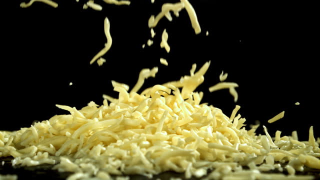 Shredded cheese falling on black background. Filmed on a high-speed camera at 1000 fps.