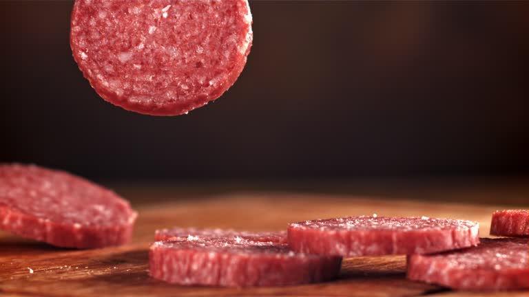 Pieces of salami fall onto a wooden board. Filmed on a high-speed camera at 1000 fps.