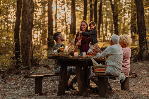 Family enjoying and having a fun time on their picnic in the woods while grandfather and grandmother are applauding to granddaughter