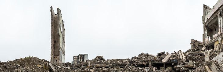 Panorama. The remains of a building with piles of gray concrete rubble and a detached ruined wall against a hazy sky. Background.