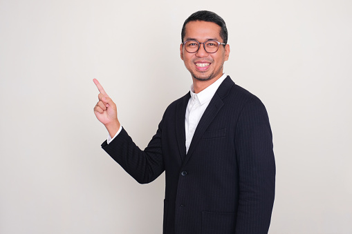 Asian businessman smiling at the camera with one hand pointing to upper right corner