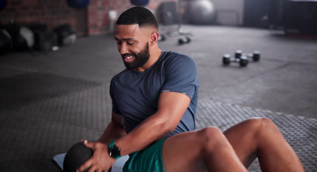 Black man, medicine ball and workout on floor for exercise, training or fitness at gym. Active African male person in crunches for muscle, strength or endurance in practice for stamina at health club
