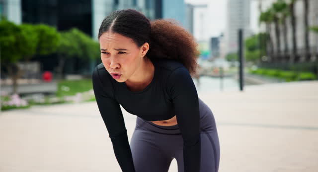Fitness, sweat and woman breathe for running in city training for race, marathon or competition. Sports, exhausted and tired female runner athlete on break for cardio workout or exercise in town.