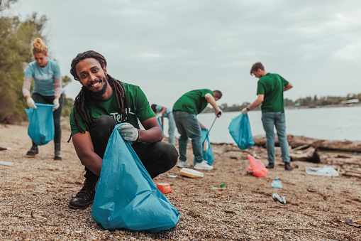 African american volunteer crouching and smiling while collecting plastic in a plastic bag on earth day