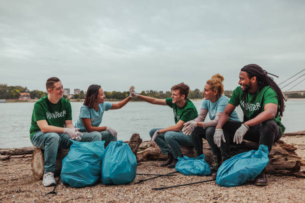 istock Five volunteers in uniforms sitting by the river doing a high five after collecting the waste 2013963479