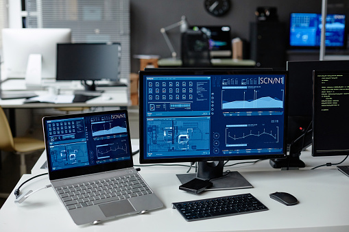 Background image of computer equipment on desk in cybersecurity office with tech data on screens copy space