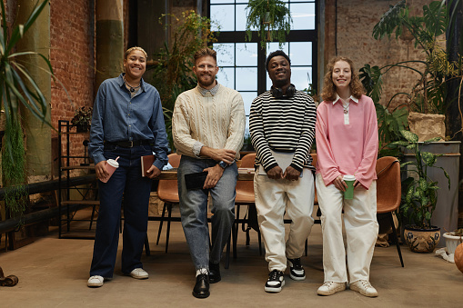 Front view full length at contemporary diverse business team smiling at camera standing in green office