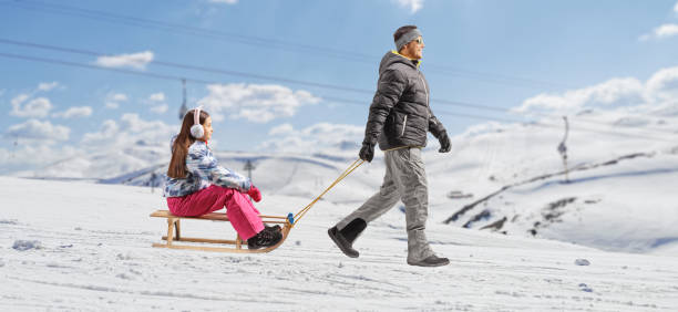 istock Man in winter clothes pulling a girl with a sled on a mountain 2013975053