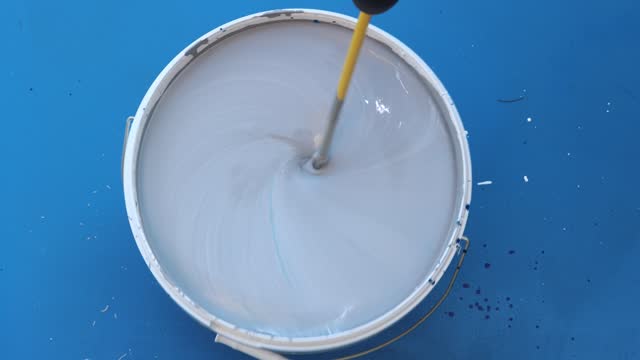 Different colors are mixed in paint bucket to get  gray with blue tint.