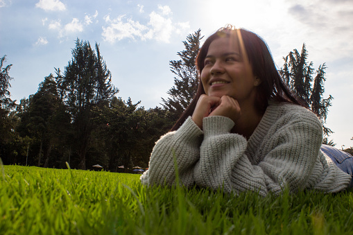 Beautiful young woman in nature lying on the grass and looking away