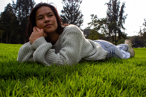 Beautiful young woman in nature lying on the grass and looking away