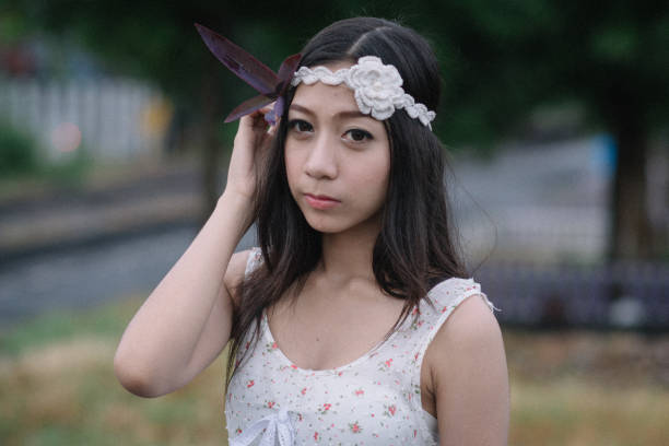 Young beautiful woman wearing white sleeveless blouse, beige pants, hat with veil at courtyard outside. White Caucasian woman looking special and fashionable 20s, 30s age. Daytime