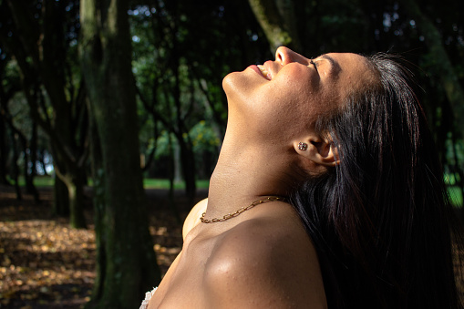 Beautiful young woman in nature smiling and eyes closed and illuminated by the sun with her hair back