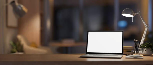 istock A modern, cozy home office at night with a white-screen laptop computer mockup on the table. 2014073983