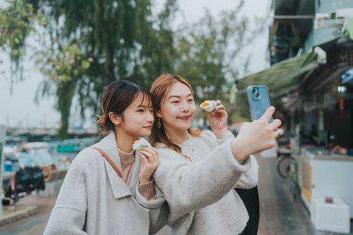 A pair of young Asian women capturing a selfie with food in hand