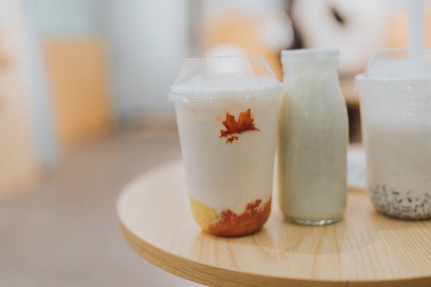 Banana smoothie in a glass next to a bunch of bananas on a light pastel pink background