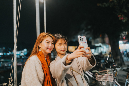 In the photo, two young asian girls are depicted taking a selfie together under the night sky in Cheung Chau, Hong Kong's outlying island