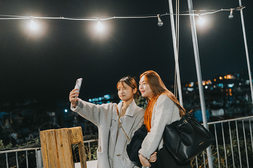 Two young asian girls are depicted taking a selfie together under the night sky in Cheung Chau, Hong Kong's outlying island