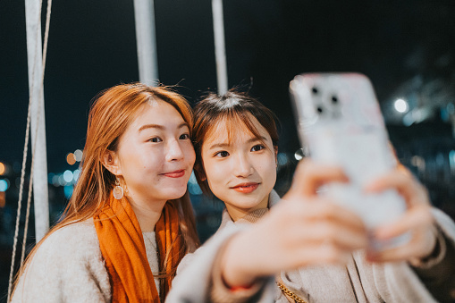 Two young asian girls are depicted taking a selfie together under the night sky in Cheung Chau, Hong Kong's outlying island