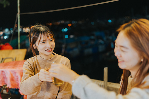 Two Young asian girl enjoying dinner at a Dai Pai Dong, an type of Hong Kong's open-air food stall. The picture features two enjoying a friendly toast together.