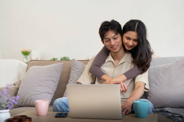 istock Young couple asian using laptop together while sitting on sofa at home 2014212037