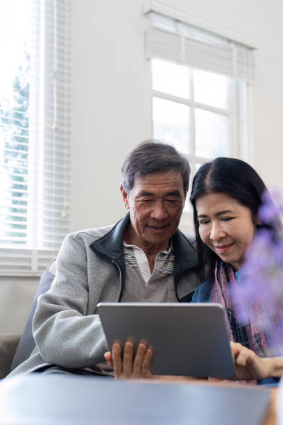 istock Happy elderly asian couple using tablet sit on sofa doing ecommerce shopping online on website and buying insurance browsing at home 2014221862