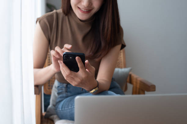 istock Smiling asian woman in casual wear using mobile phone while working on laptop computer at coffee shop. Young woman freelancer online working and using smartphone, surfing internet, people lifestyle 2014291398