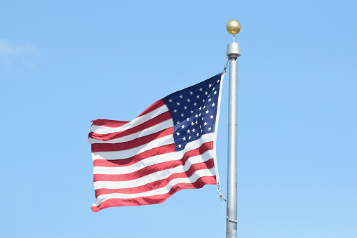 The flag of the United States of America flies from a flagpole in this vertical orented photograph with great detail and vibrant colors.
