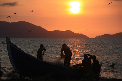 On the coast of Banda Aceh on  04/08/2020,  A group of fishermen from the Javanese village skillfully cleaned their nets. Amidst the sunset ambiance, they employed the traditional method of shore seine to catch fish. Their hands moved skillfully and systematically, clearing debris and repairing the nets. The twilight light enhanced their silhouettes, creating a beautiful portrayal of fishermen's lives deeply intertwined with the sea.