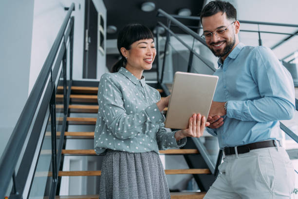 Business colleagues talking on stairs in the office. Shot of two colleagues using a digital tablet while walking down stairs in a modern office. Two business people in a motion on stairs in the office. ladder of success stock pictures, royalty-free photos & images