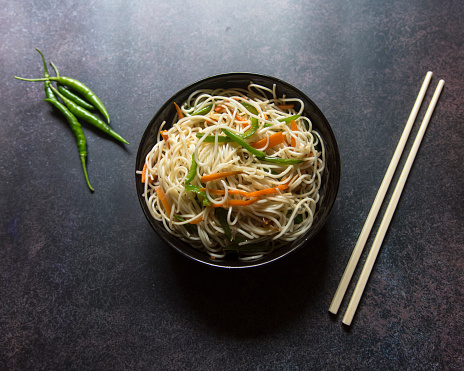 Top view of vegetable schezwan noodles or vegetable hakka noodles or chow mein in a black bowl